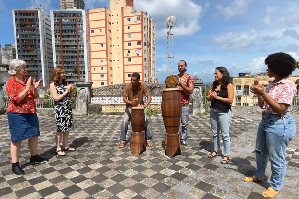 A group of 6 people, 2 playing instruments and 4 clapping, in South America 